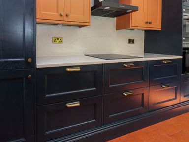 A kitchen countertop with dark blue cabinets orange upper cabinets and a stove at Bryn Tirion in Morfa Nefyn