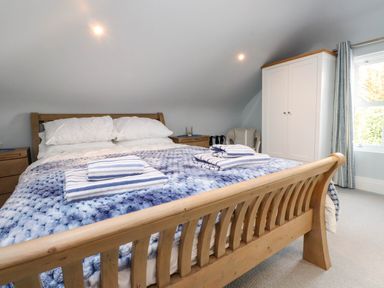A bedroom with a wooden bed and blue blanket with striped towels on top at Bryn Tirion in Morfa Nefyn