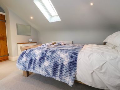 A bedroom with a bed covered in white bedding and a blue patterned throw under a skylight at Bryn Tirion in Morfa Nefyn