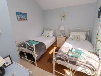 A bedroom with two single metal frame beds a nightstand lamp and wall decor at Bryn Tirion in Morfa Nefyn