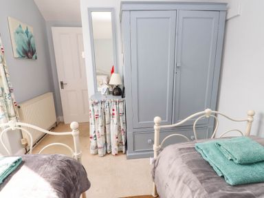 A bedroom with two single beds gray wardrobe and a radiator at Bryn Tirion in Morfa Nefyn