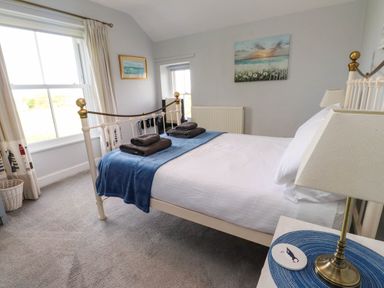 A bedroom with a bed covered by blue and white bedding and towels on top at Bryn Tirion in Morfa Nefyn