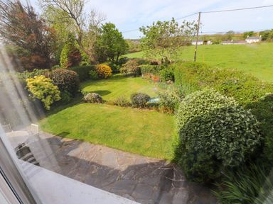 A garden with grass lawn shrubs trees a stone patio and outdoor chairs at Bryn Tirion in Morfa Nefyn