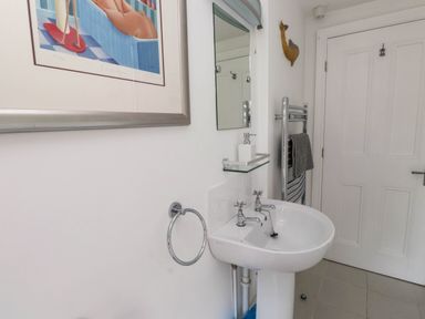 A bathroom with a white sink pedestal faucets mirror towel rack and framed artwork at Bryn Tirion in Morfa Nefyn
