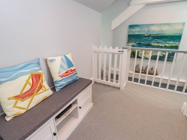 A landing area with a bench with cushions and a safety gate near a railing with a painting of boats at Bryn Tirion in Morfa Nefyn