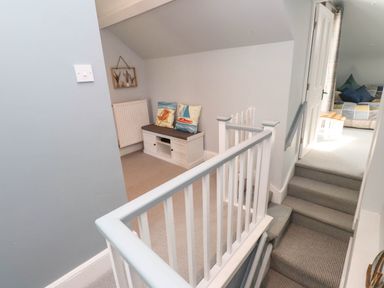 A stairway landing with a white bench with cushions and a partially visible room with a sofa at Bryn Tirion in Morfa Nefyn