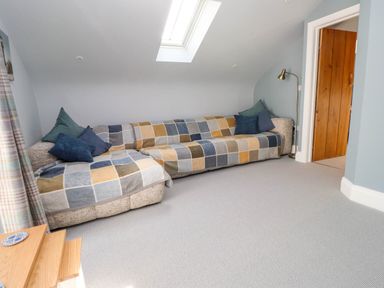 A living room with a patchwork patterned sofa under a skylight window and a wooden door at Bryn Tirion Morfa Nefyn