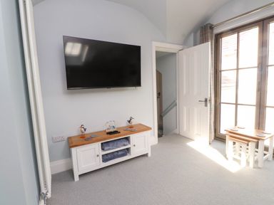 A room with a wall mounted television a white cabinet two bird figurines a door and a window at Bryn Tirion in Morfa Nefyn