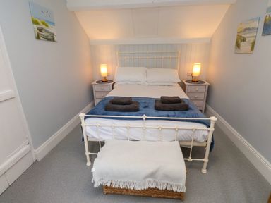 A bedroom with a double bed two bedside tables with lamps a wicker basket with a blanket at Bryn Tirion in Morfa Nefyn