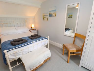 A bedroom with a white metal bed frame a bedside table with a lamp a wooden chair a full-length mirror and framed pictures on the wall at Bryn Tirion in Morfa Nefyn