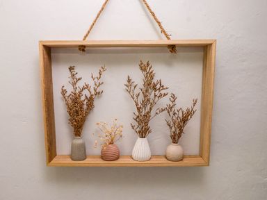 A wooden frame hanging on a wall holding four small vases with dried flowers inside at Bryn Tirion in Morfa Nefyn
