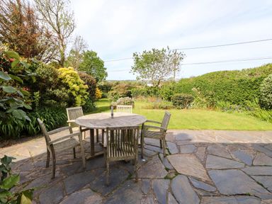 A garden with a stone patio and a round wooden table with four wooden chairs at Bryn Tirion in Morfa Nefyn