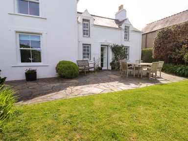 A patio with outdoor furniture and plants in front of a white house at Bryn Tirion in Morfa Nefyn