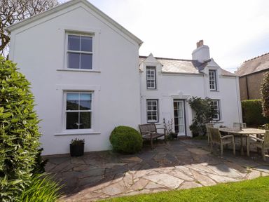 A white house with stone patio and outdoor wooden furniture at Bryn Tirion in Morfa Nefyn