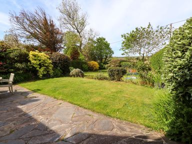 An outdoor garden area with a stone patio lawn trees and shrubs at Bryn Tirion in Morfa Nefyn