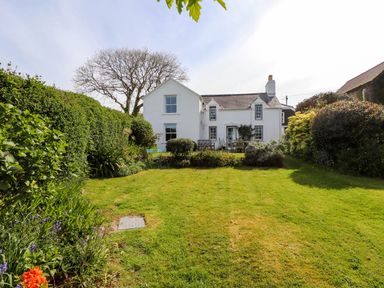 A grassy garden with shrubs and outdoor furniture in front of a white house at Bryn Tirion in Morfa Nefyn
