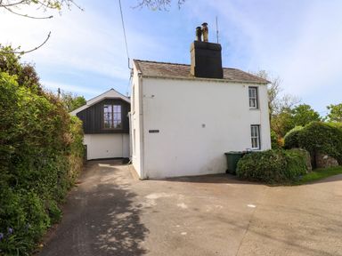 A driveway leading to a white house with a garage and greenery around at Bryn Tirion in Morfa Nefyn