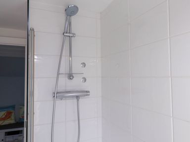 A shower head and controls attached to tiled wall in a bathroom at Bryn Tirion in Morfa Nefyn