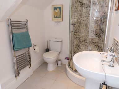 A bathroom with a toilet, curved glass shower, white sink, chrome towel rack with a blue towel at Bryn Tirion in Morfa Nefyn