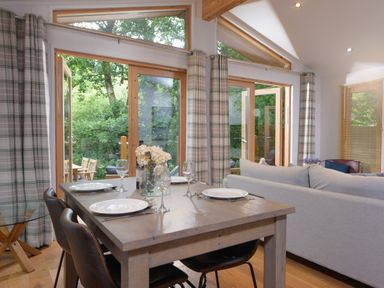 A dining table set for four next to large windows with open doors and a grey sofa in Lanreath near Looe