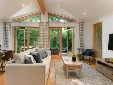 A living room with a beige sofa and wooden coffee table facing glass doors with curtains at 10 Stonerush Valley Lanreath near Looe