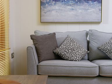 A gray sofa with three patterned cushions under a blue and white painting at 10 Stonerush Valley Lanreath near Looe