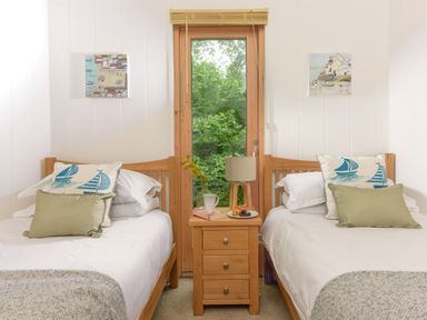 A bedroom with two single beds separated by a wooden nightstand under a window with a garden view at 10 Stonerush Valley Lanreath near Looe