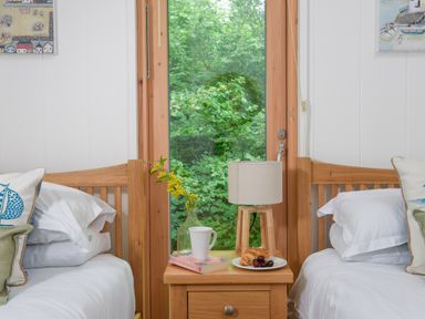 A bedroom with two single wooden beds and a wooden nightstand holding a lamp book mug vase and plate with food at 10 Stonerush Valley Lanreath near Looe