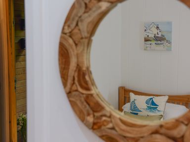 A wooden bed with nautical-themed pillows and a coastal painting on the wall reflected in a round wooden mirror at 10 Stonerush Valley Lanreath near Looe