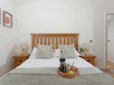 A bedroom with a wooden bed frame white bedding two side tables with lamps and a breakfast tray at 10 Stonerush Valley Lanreath near Looe