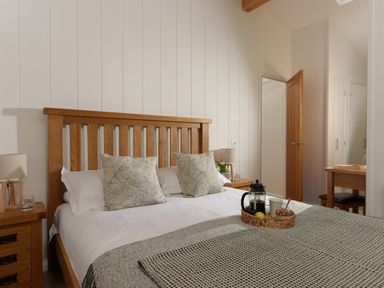 A bedroom with a wooden bed frame two pillows a bedside table with a lamp and a tray with coffee and fruit at 10 Stonerush Valley Lanreath near Looe