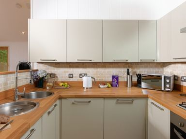 A kitchen with wooden countertops, light-colored cabinets, a stainless steel sink, a microwave, a kettle, and fruit on the counter at 10 Stonerush Valley Lanreath near Looe