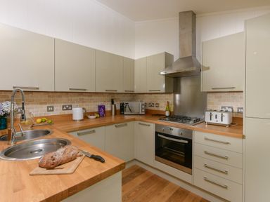 A kitchen with wooden countertops beige cabinets a stainless steel oven and stove a toaster a microwave a knife set and bread on a cutting board at 10 Stonerush Valley in Lanreath near Looe
