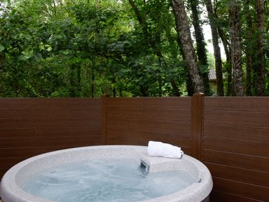 An outdoor hot tub with water and a white towel on the edge surrounded by a wooden fence and trees at 10 Stonerush Valley Lanreath near Looe
