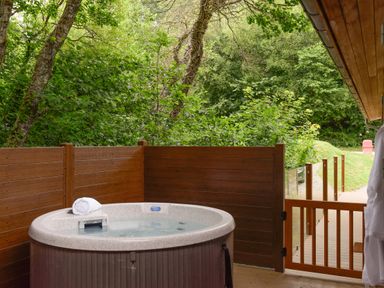 An outdoor hot tub with a towel on the edge surrounded by wooden fencing and trees at 10 Stonerush Valley Lanreath near Looe