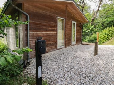 An exterior view of a wooden building with gravel ground and an electric vehicle charging station in a green area