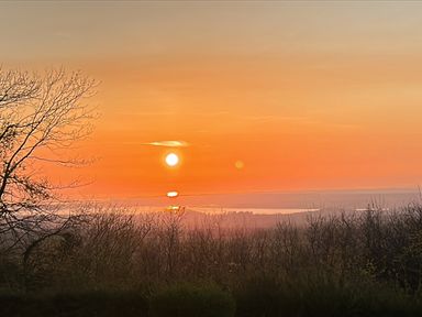 A sunset view with trees and water at Tan Y Merddyn in Ceunant near Llanrug