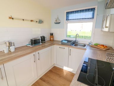 A kitchen with wooden countertops a black toaster a kettle a sink with a dish rack and a window with blue anchor blinds at The Sail Loft in Norton Park near Dartmouth