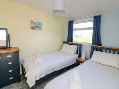 A bedroom with two single beds a chest of drawers and a window with blue curtains at The Sail Loft Norton Park near Dartmouth
