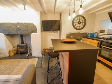 A kitchen area with a black stove and oven a black countertop with two stools blue toaster and kettle a wall clock and a wall-mounted television at Ty Dyffryn in Llan Ffestiniog