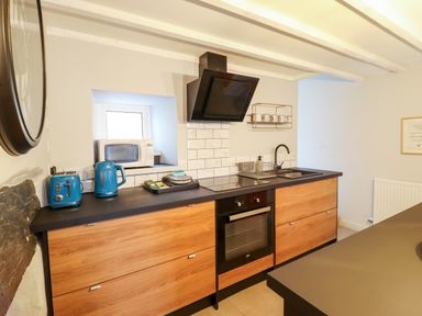 A kitchen with wooden cabinets black countertop blue toaster and kettle oven and black sink at Ty Dyffryn in Llan Ffestiniog