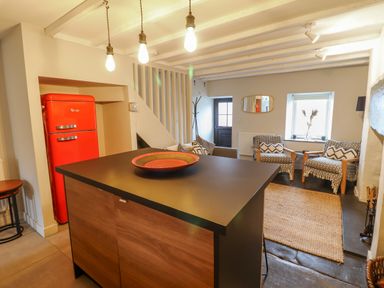 A kitchen island with a red bowl and a red fridge near a sitting area with patterned armchairs and a woven rug at Ty Dyffryn in Llan Ffestiniog