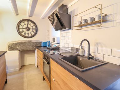 A kitchen with wooden cabinets a black countertop a sink a drying rack blue toaster and kettle a wall clock and a microwave at Ty Dyffryn in Llan Ffestiniog