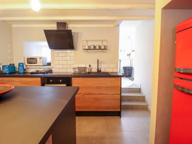 A kitchen with wooden cabinets a black countertop a black stove a black hood a red refrigerator and a microwave at Ty Dyffryn in Llan Ffestiniog