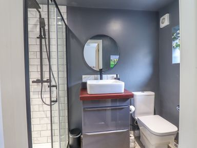 A bathroom with a shower, sink with a round mirror, and a toilet at Ty Dyffryn in Llan Ffestiniog
