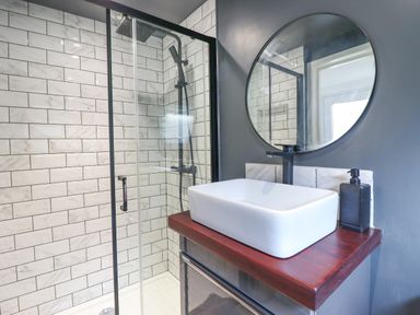 A bathroom with a glass shower enclosure white rectangular sink wooden countertop and round mirror at Ty Dyffryn in Llan Ffestiniog