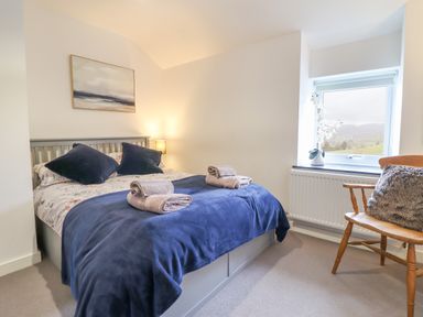 A bedroom with a bed covered in blue bedding towels on the bed a wooden chair with a cushion and a window with a view at Ty Dyffryn in Llan Ffestiniog