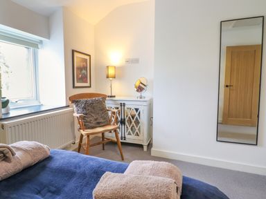A bedroom with a wooden chair and cushion beside a white cabinet with a lamp and mirror and a wall mirror at Ty Dyffryn in Llan Ffestiniog