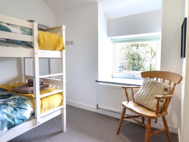 A bedroom with a white bunk bed and a wooden chair next to a window at Ty Dyffryn in Llan Ffestiniog