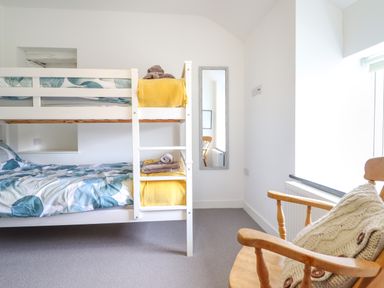 A bedroom with a white bunk bed and a wooden chair with a cushion at Ty Dyffryn in Llan Ffestiniog
